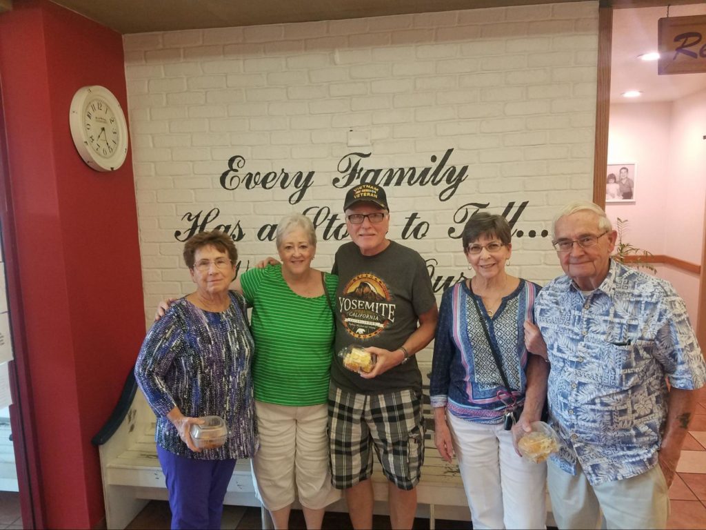 A group of diners at Brookfields Restaurant in front of a sign that says: “Every family has a story to tell…this is ours.”