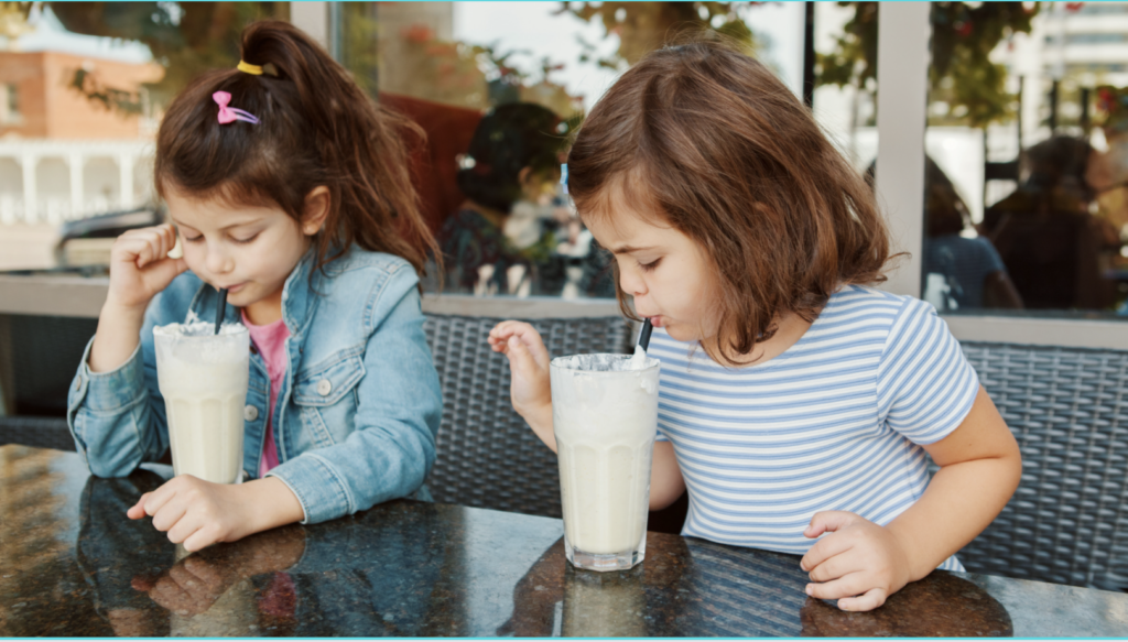 Two girls sitting at a restaurant booth sipping milkshakes.