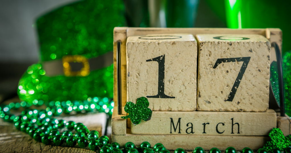 A block calendar with March 17th written on it, and festive shamrocks and other green decor in the background.