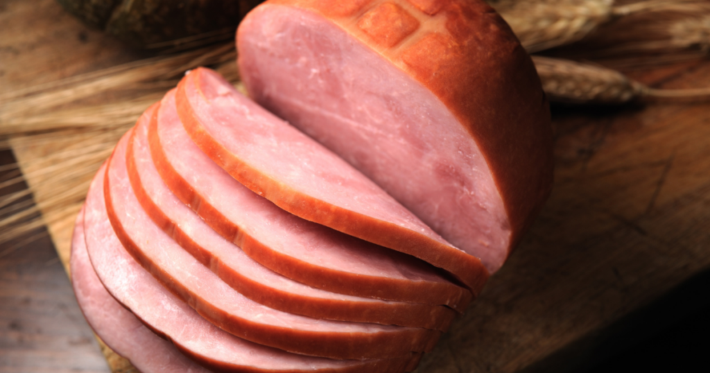 Alt Text: A sliced ham on a wooden board.