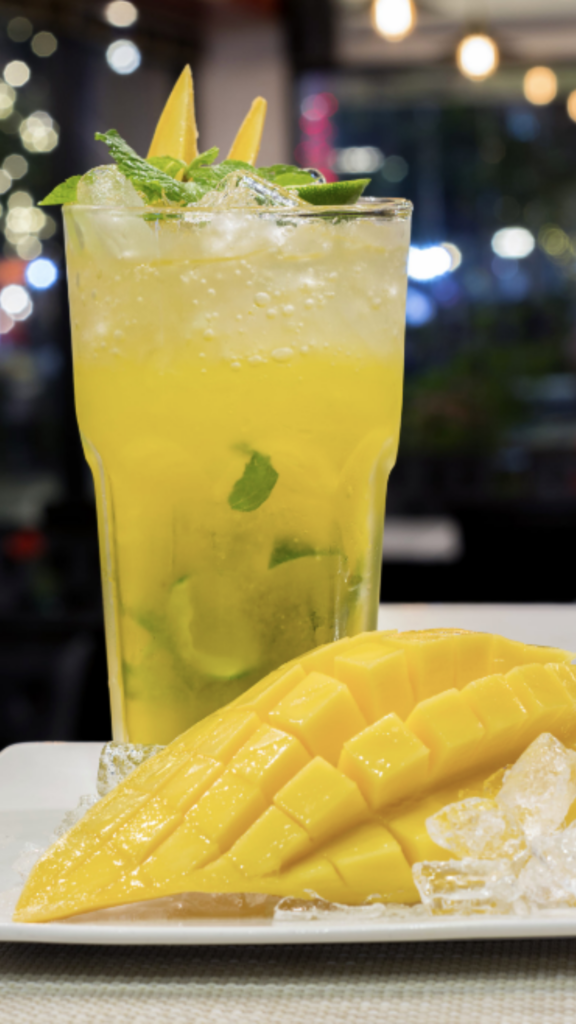 A yellow mango signature cocktail behind fresh-cut mango.
