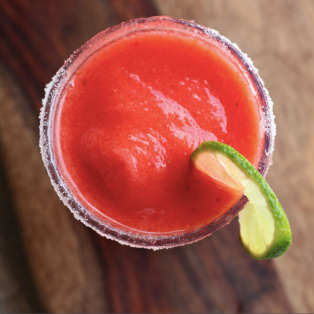 A bright red blended strawberry drink garnished with lime.
