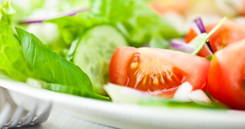 A close up of a summer salad complete with red onions, tomatoes, cucumbers, and mixed greens.